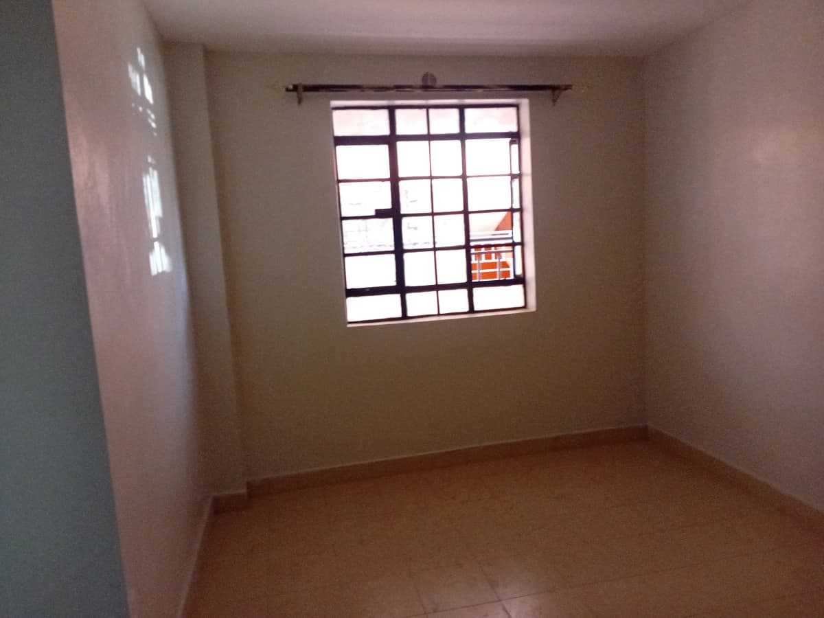 Empty bedroom with barred window and terracotta tile floor