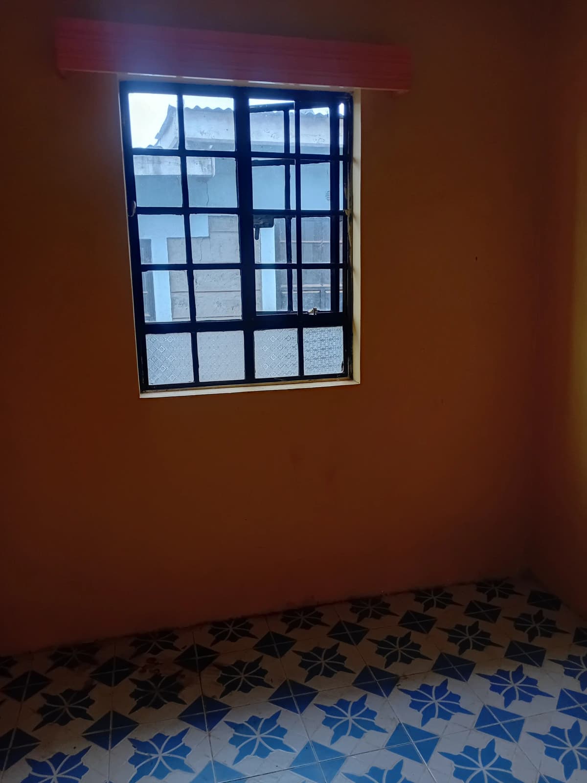 Modest bedroom with barred window and patterned tile floor