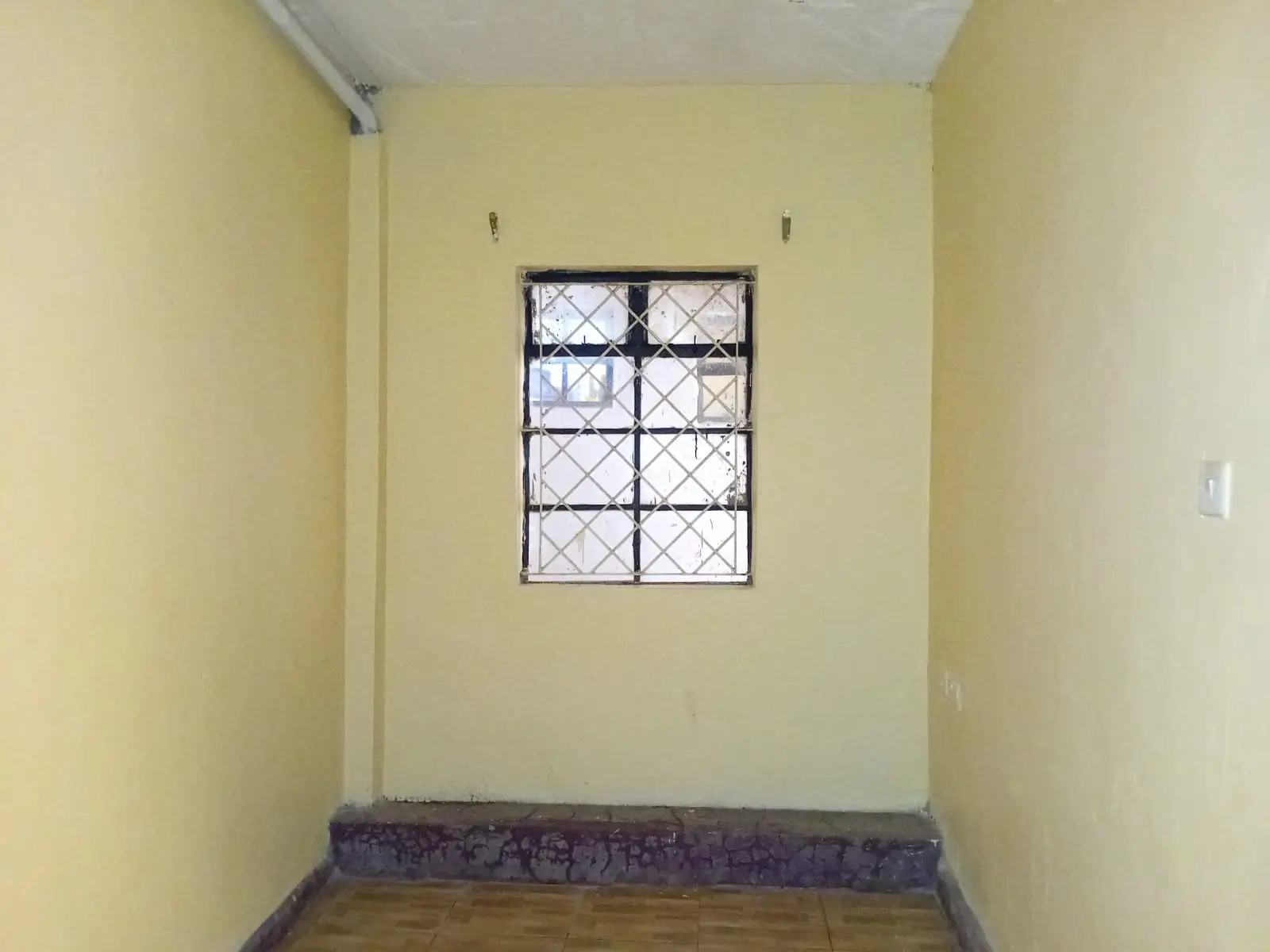 Compact bedroom with barred window and yellow walls