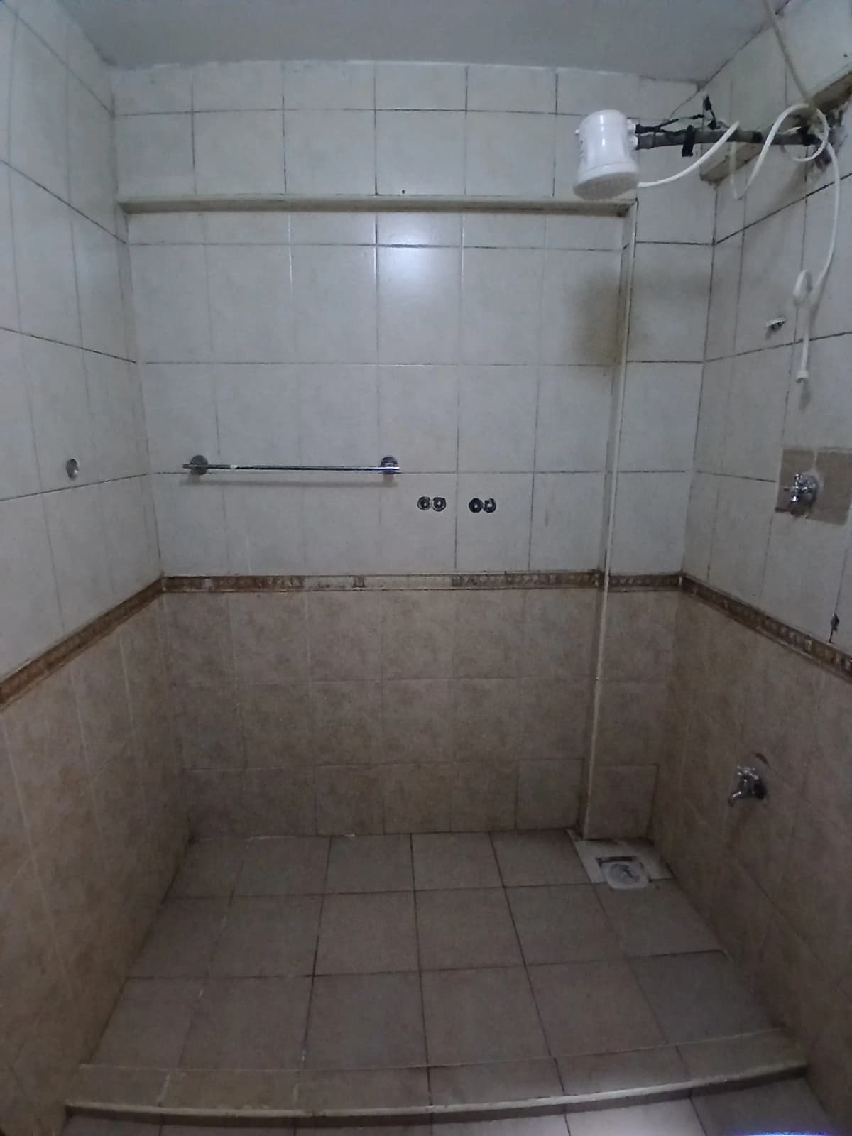 Empty bathroom with white tile walls, shower area, floor fixtures