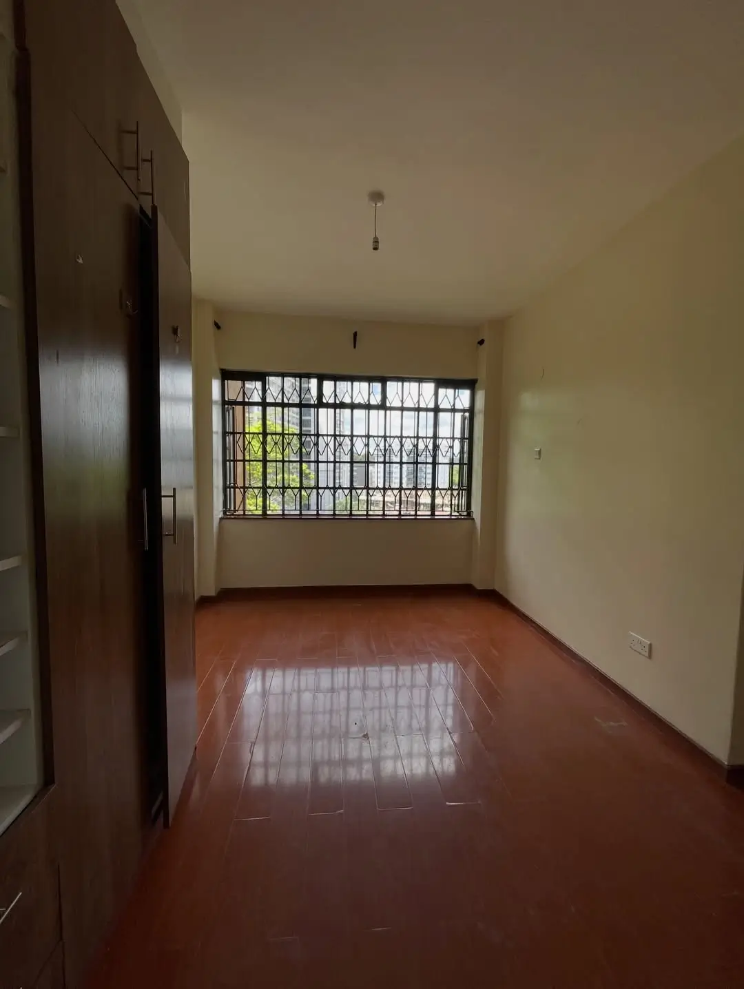 Spacious bedroom with wooden floor and barred window