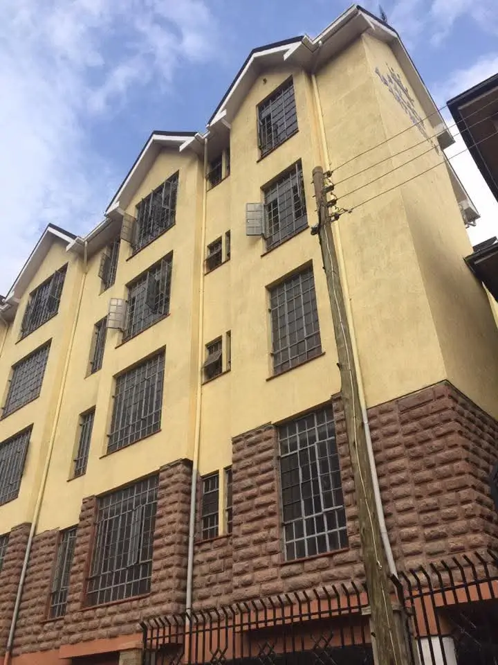 Yellow multi-story residential building with brick base and gated entrance