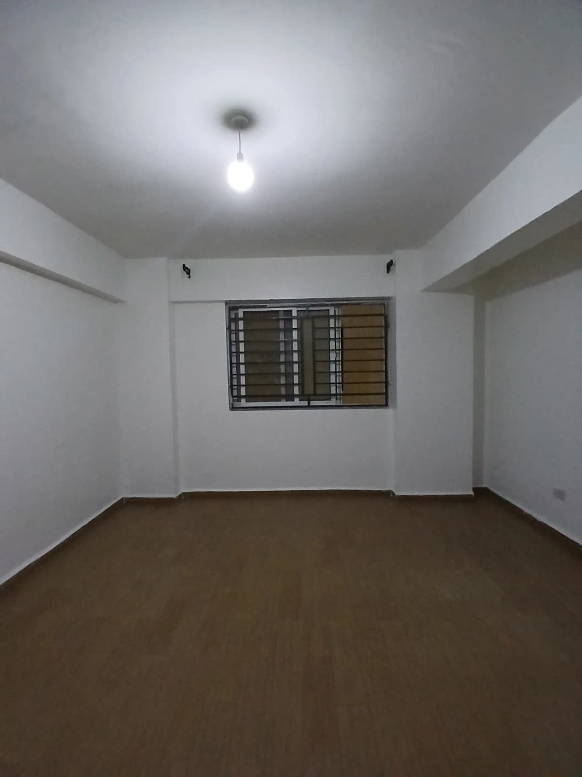 Empty bedroom with brown tile floor and barred window