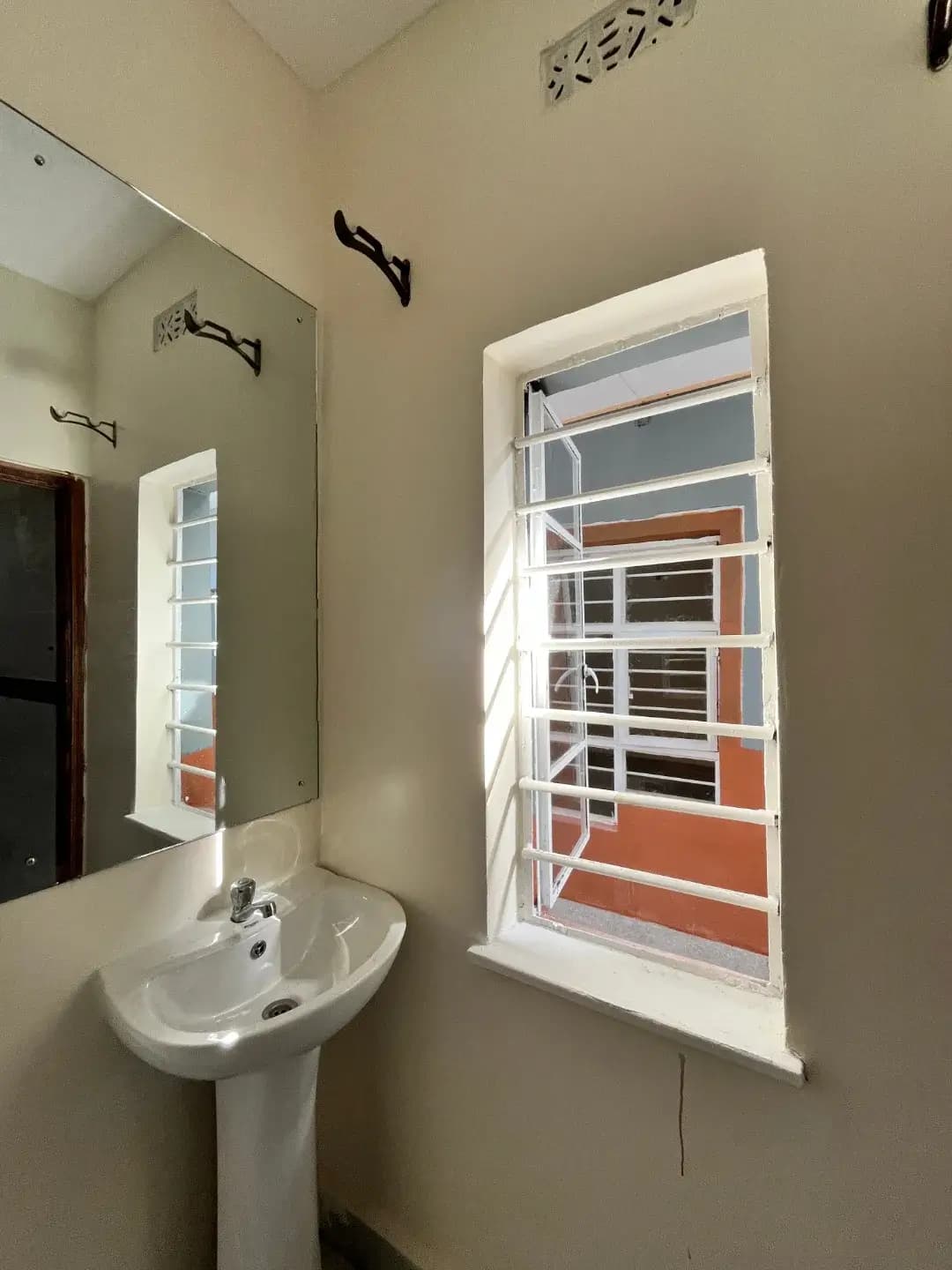 Compact bathroom with pedestal sink and louvered window