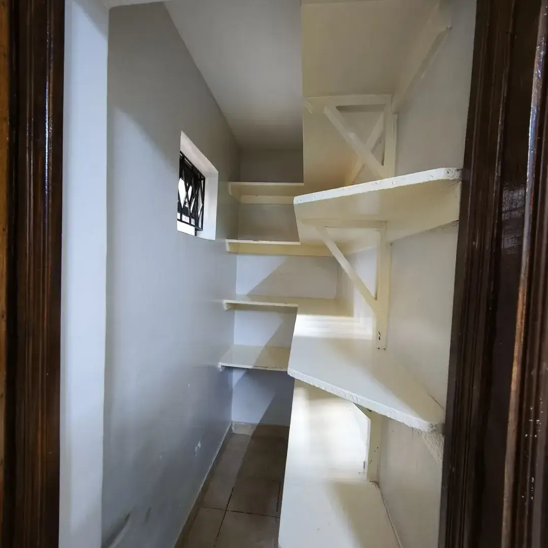 Empty pantry with white shelving units and dark door frame.