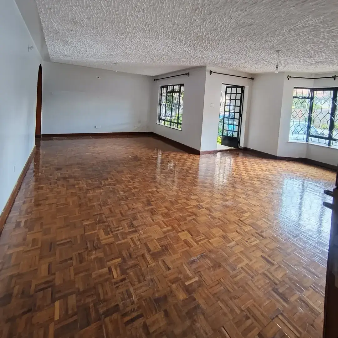 Spacious empty living room with parquet flooring and natural light.