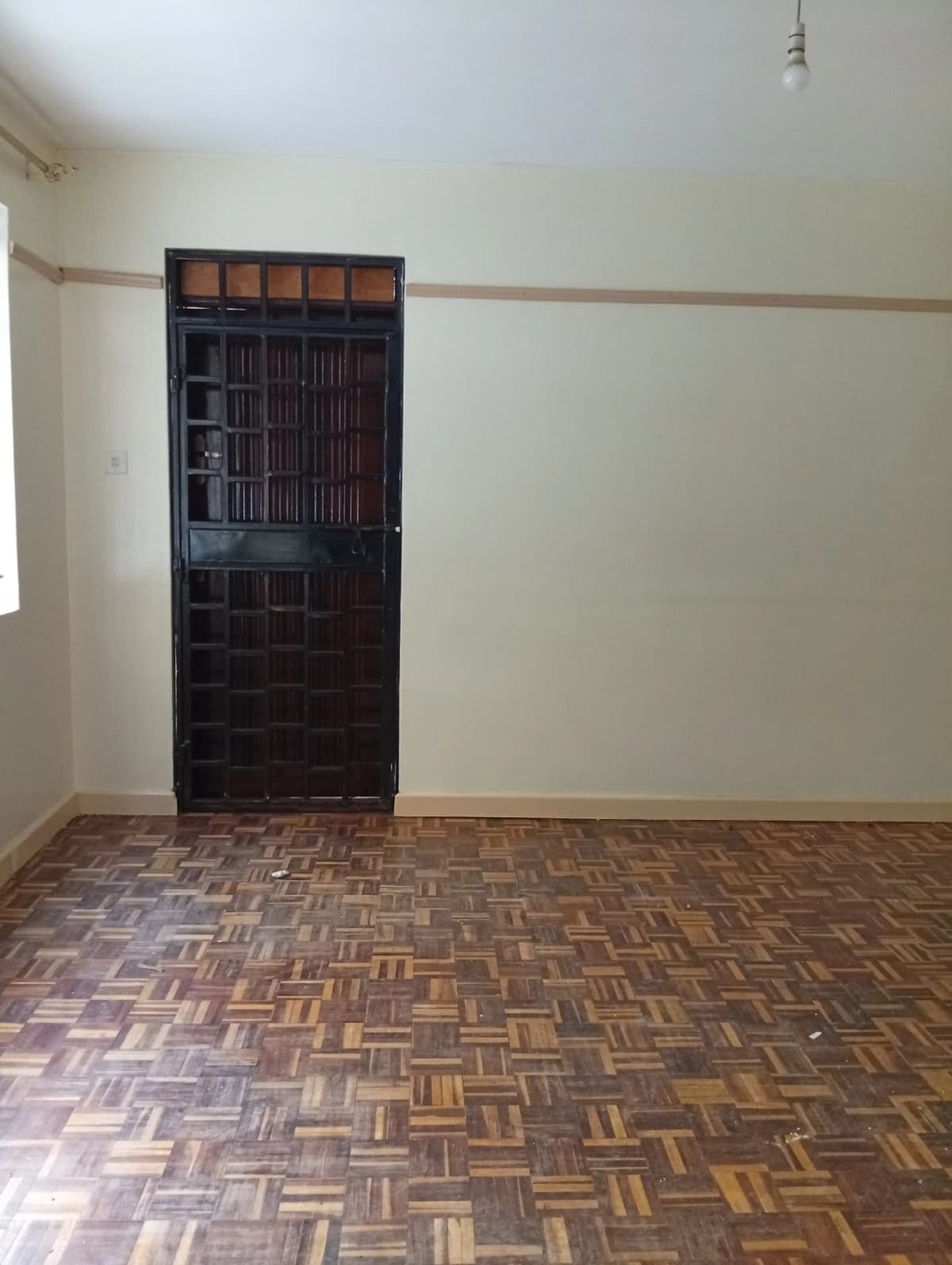 Empty bedroom with herringbone wood flooring and dark wooden door
