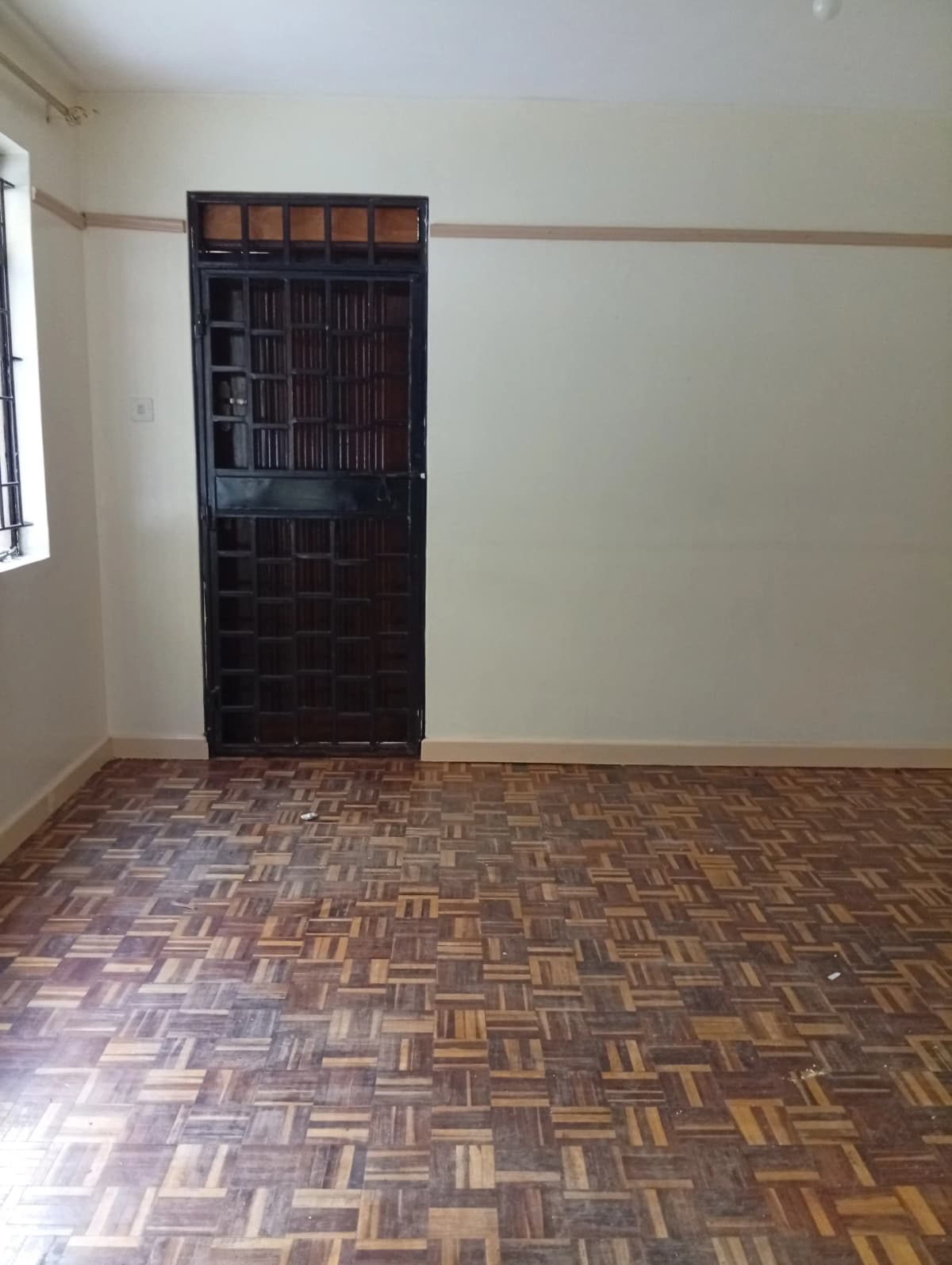 Empty bedroom with herringbone parquet flooring and dark wooden door