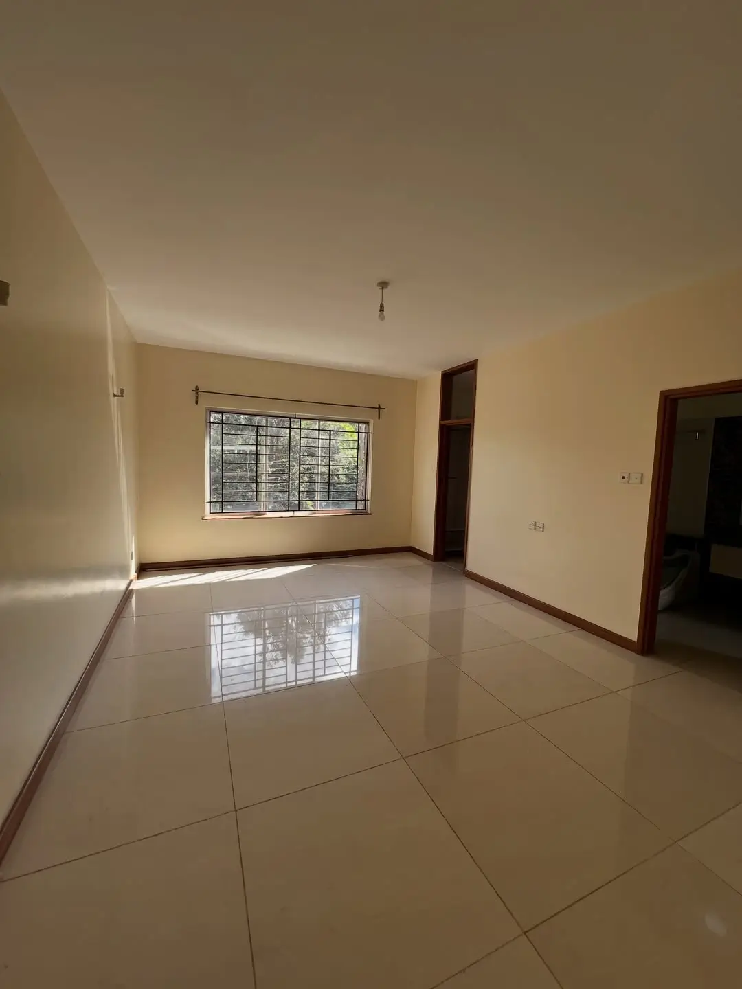Spacious empty living room with polished tile flooring and barred window