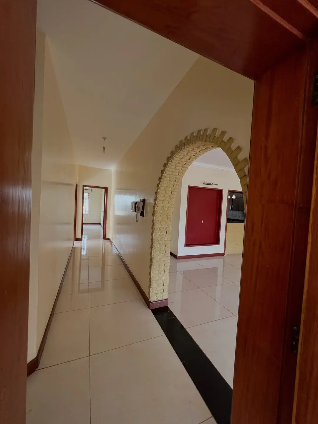 Hallway with brick archway, cream walls, red door entrance