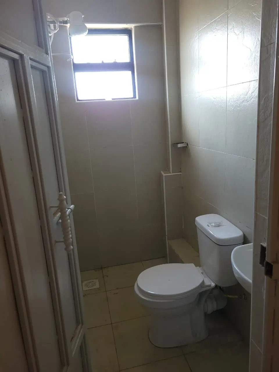 Compact bathroom with toilet, sink, window, shower enclosure