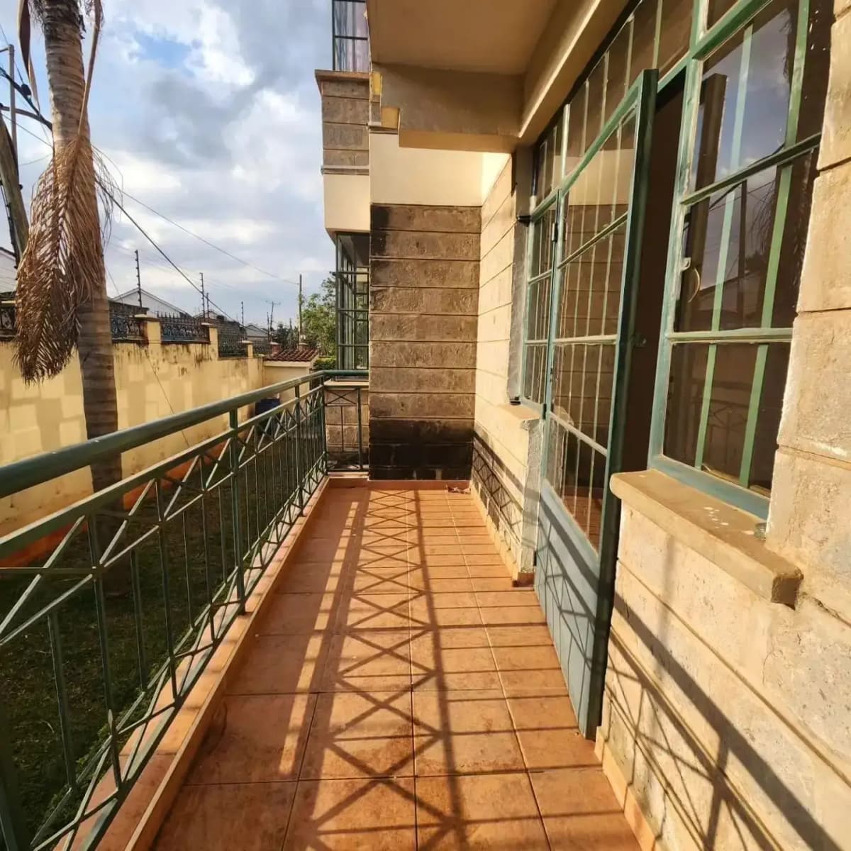Long covered balcony with terracotta tiles and green railing