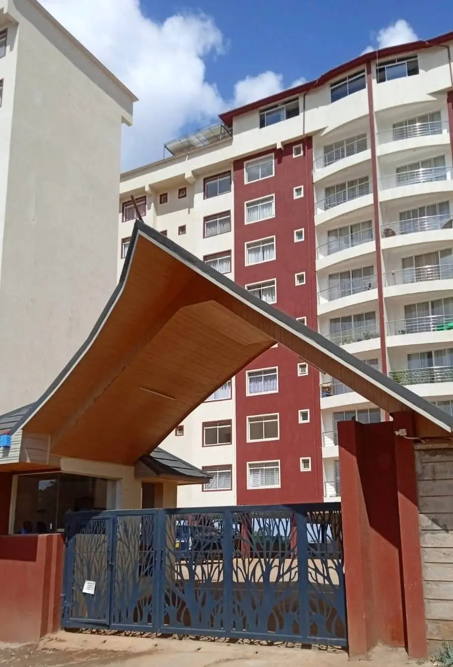 Modern apartment complex with red and white facade, gated entrance