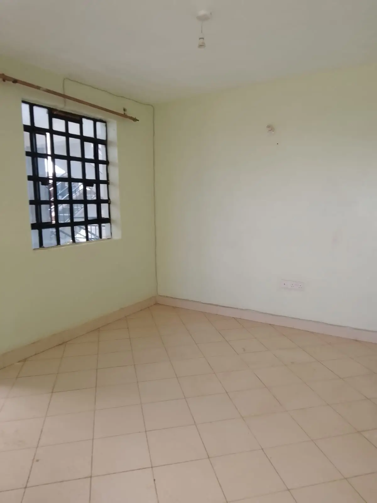 Empty bedroom with barred window and terracotta tile flooring