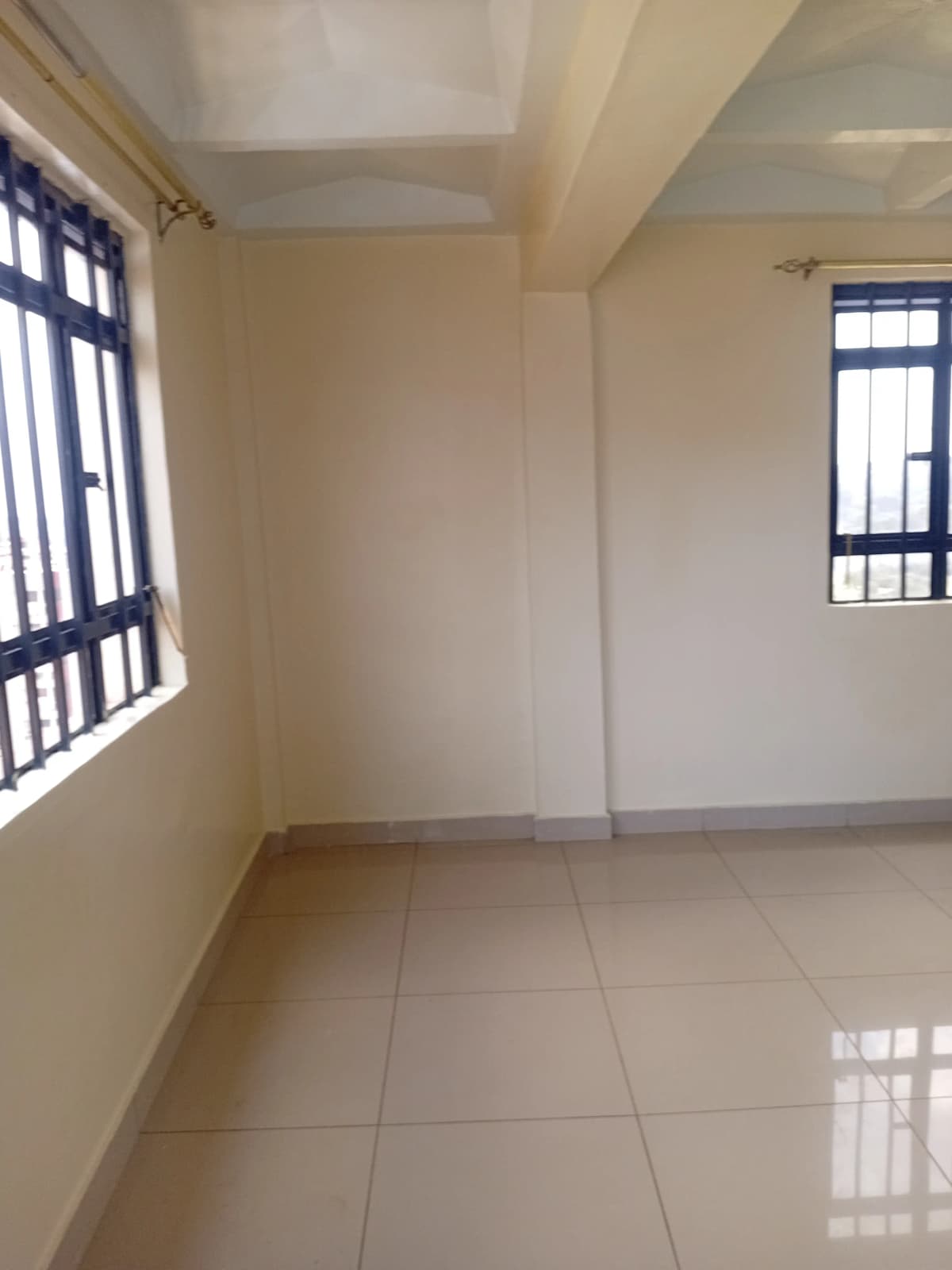 Spacious empty bedroom with tiled flooring and barred windows