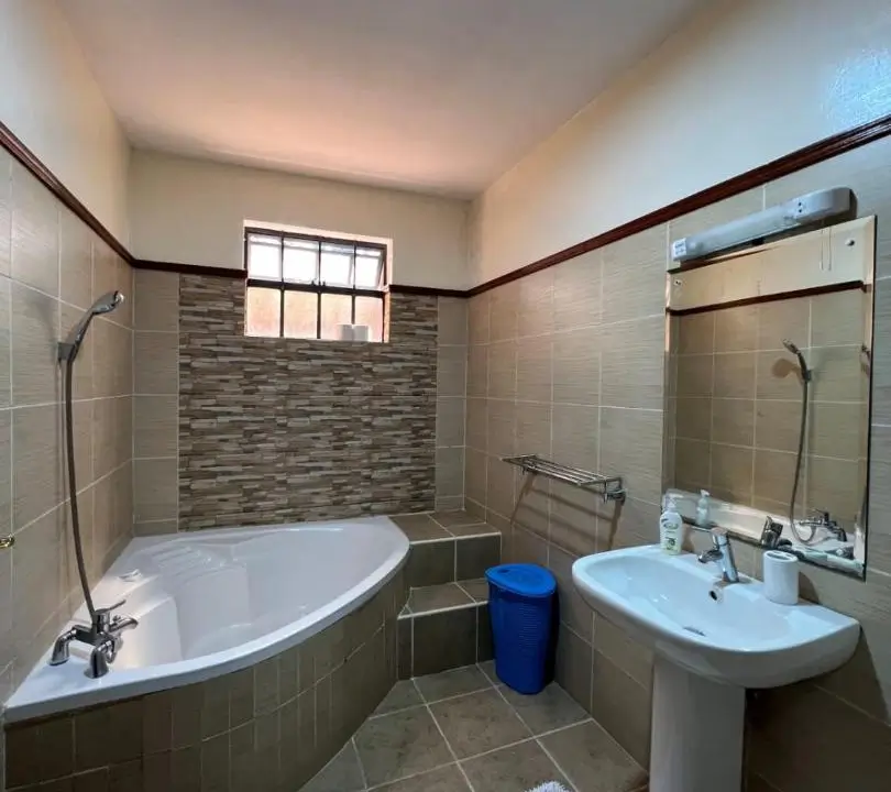 Spacious bathroom with corner bathtub, pedestal sink, and tiled walls