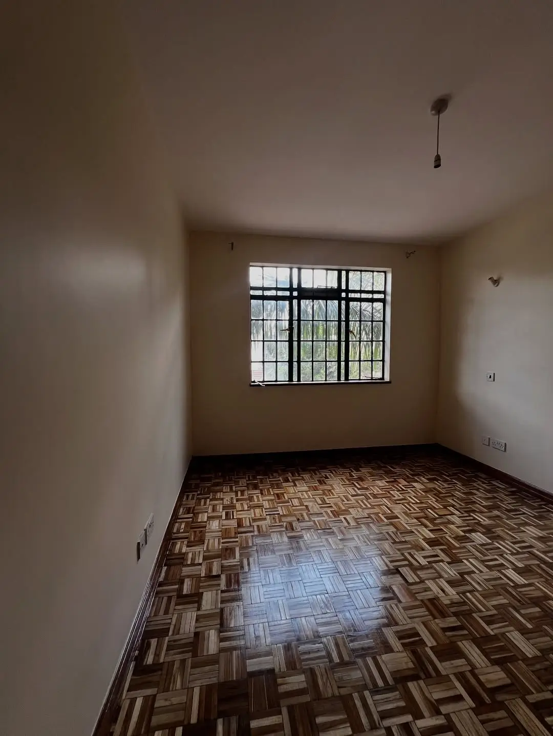 Empty bedroom with barred window and parquet flooring