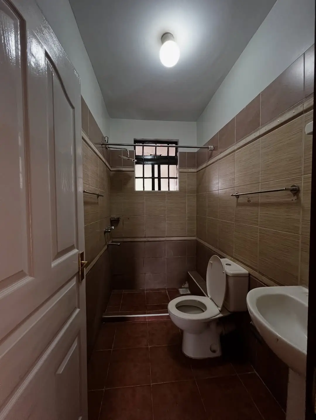 Brown-tiled bathroom with toilet, sink, and shower cubicle