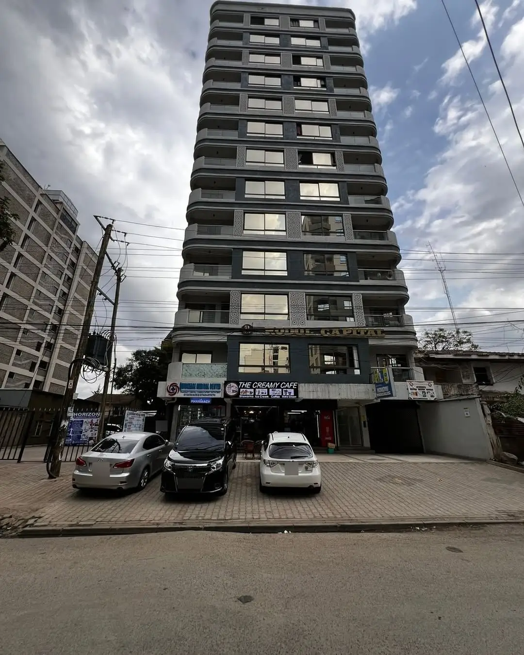 Ground-level parking area with multiple vehicles and tall residential building