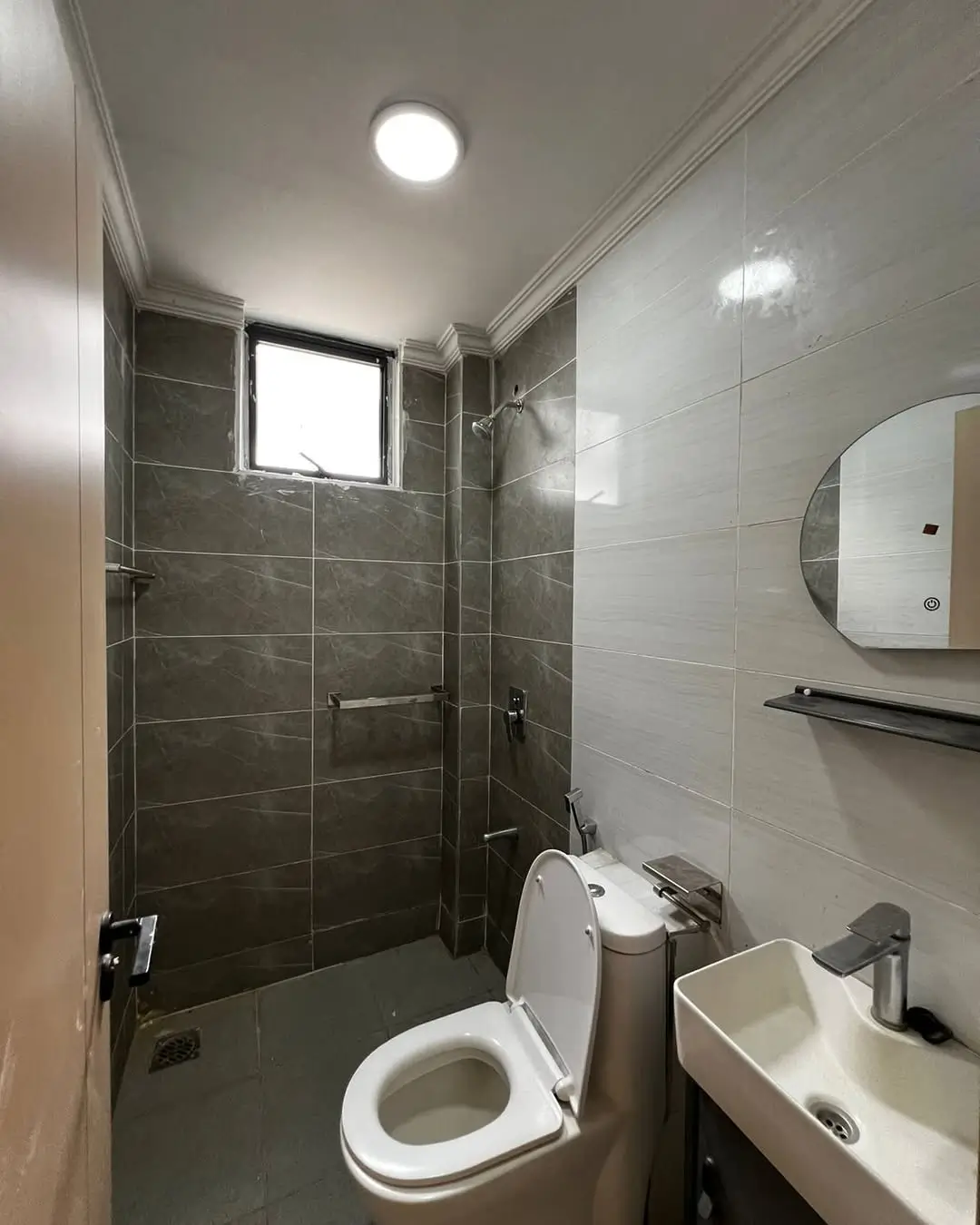 Modern bathroom with dark tile shower, toilet, and round mirror