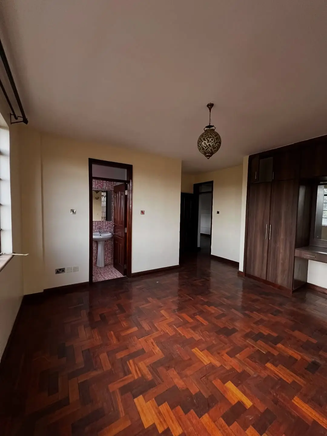 Spacious ensuite bedroom with herringbone wood flooring and pendant light