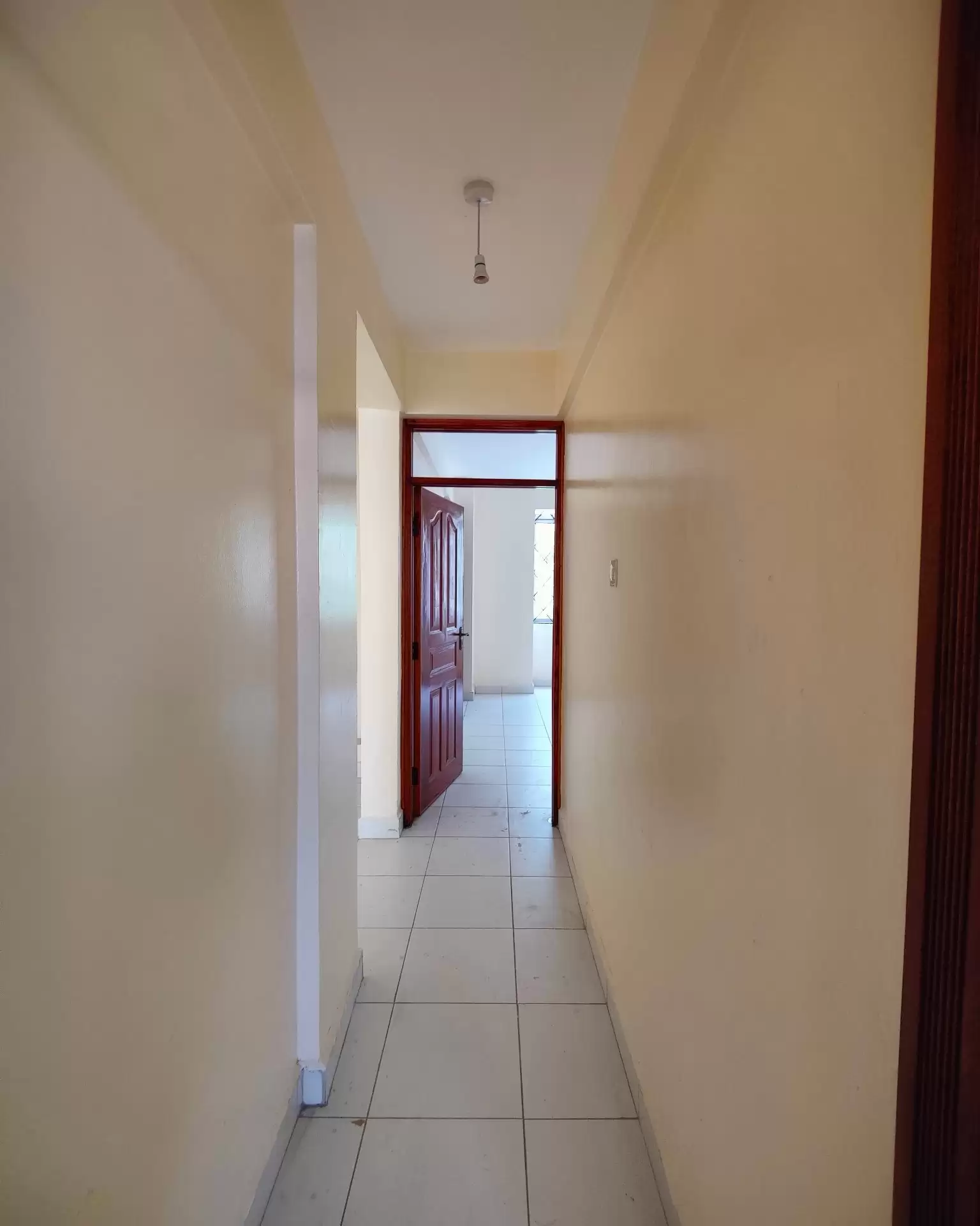 Long narrow hallway with tile flooring and cream walls