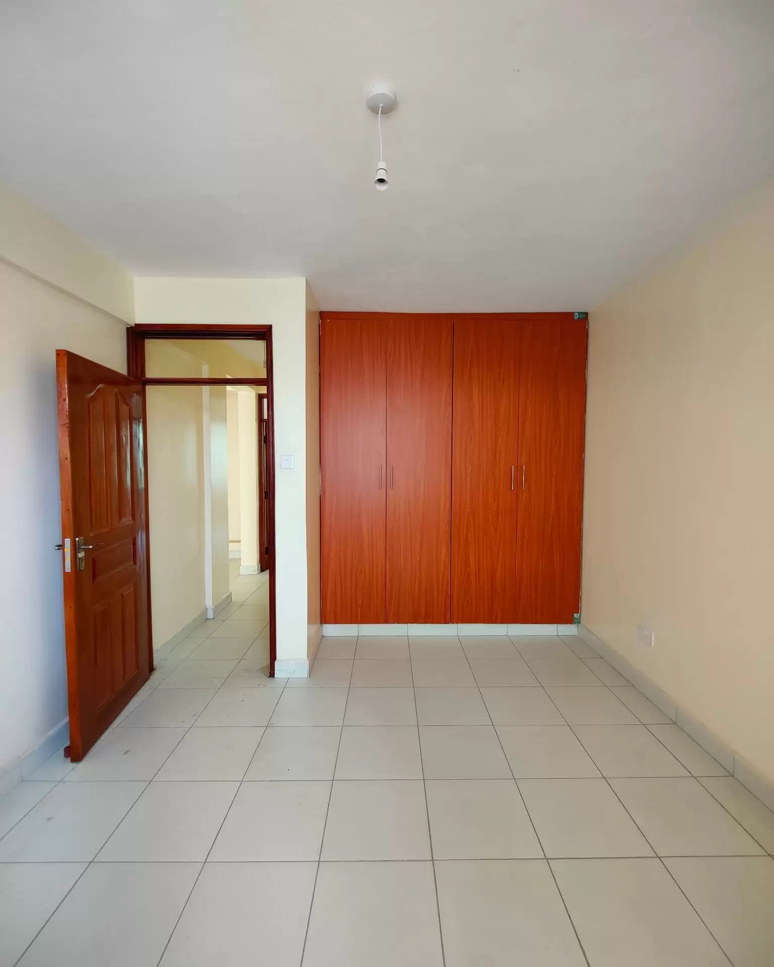 Empty bedroom with tile flooring and wooden wardrobe doors