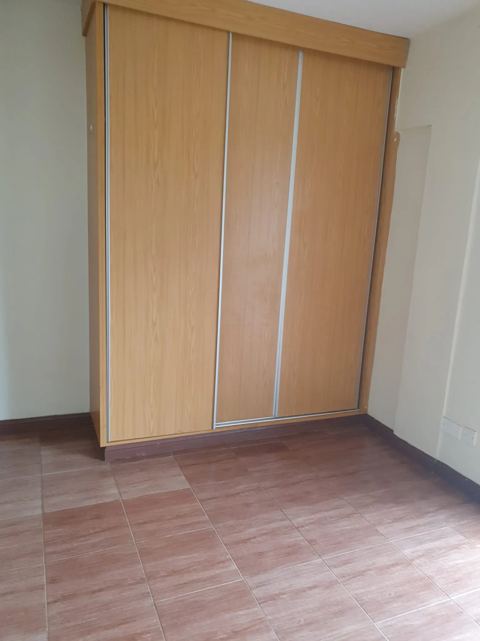 Empty bedroom with built-in wooden wardrobe and tiled floor