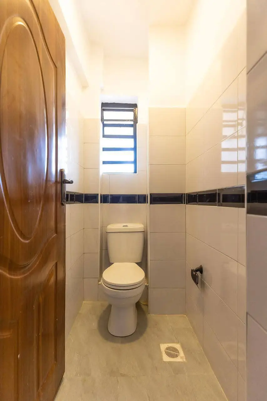 Compact bathroom with toilet, tile walls, and high window