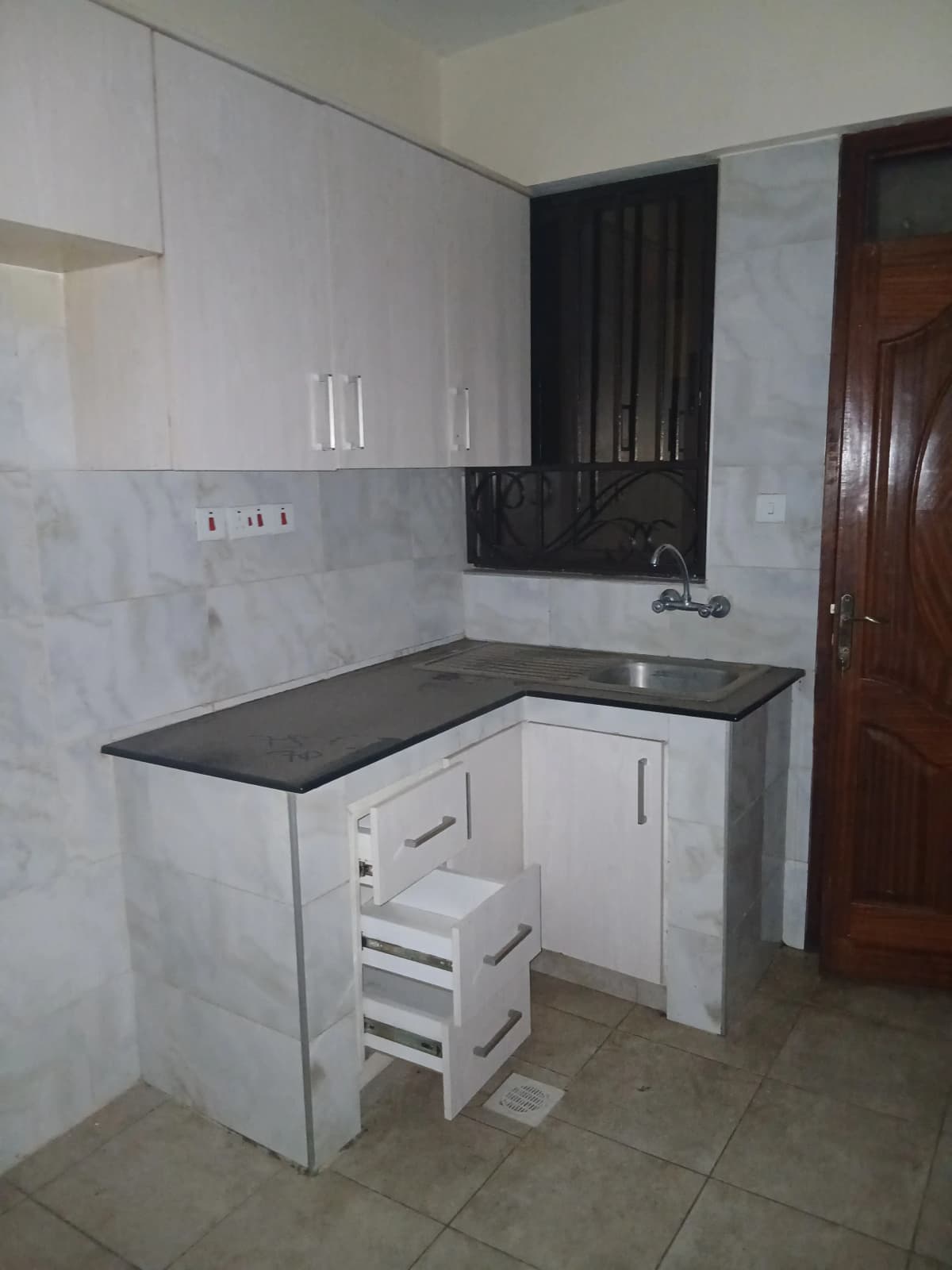 Compact L-shaped kitchen with white cabinets, black countertop