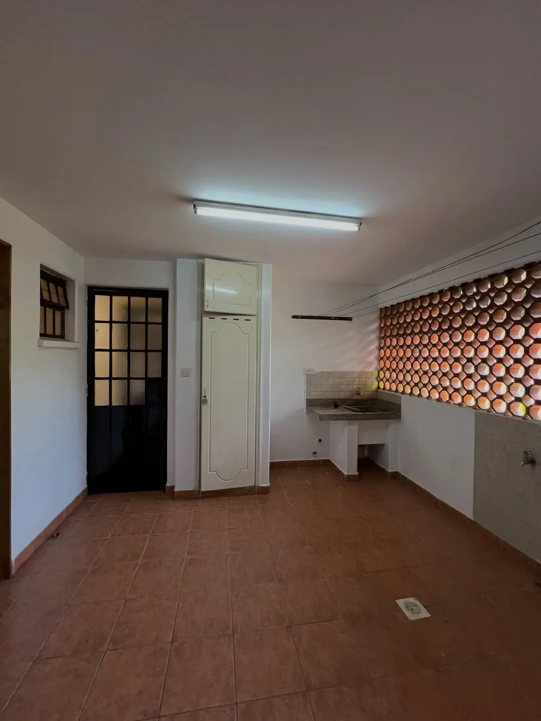 Compact laundry area with terracotta tiles, sink wash area and ventilation