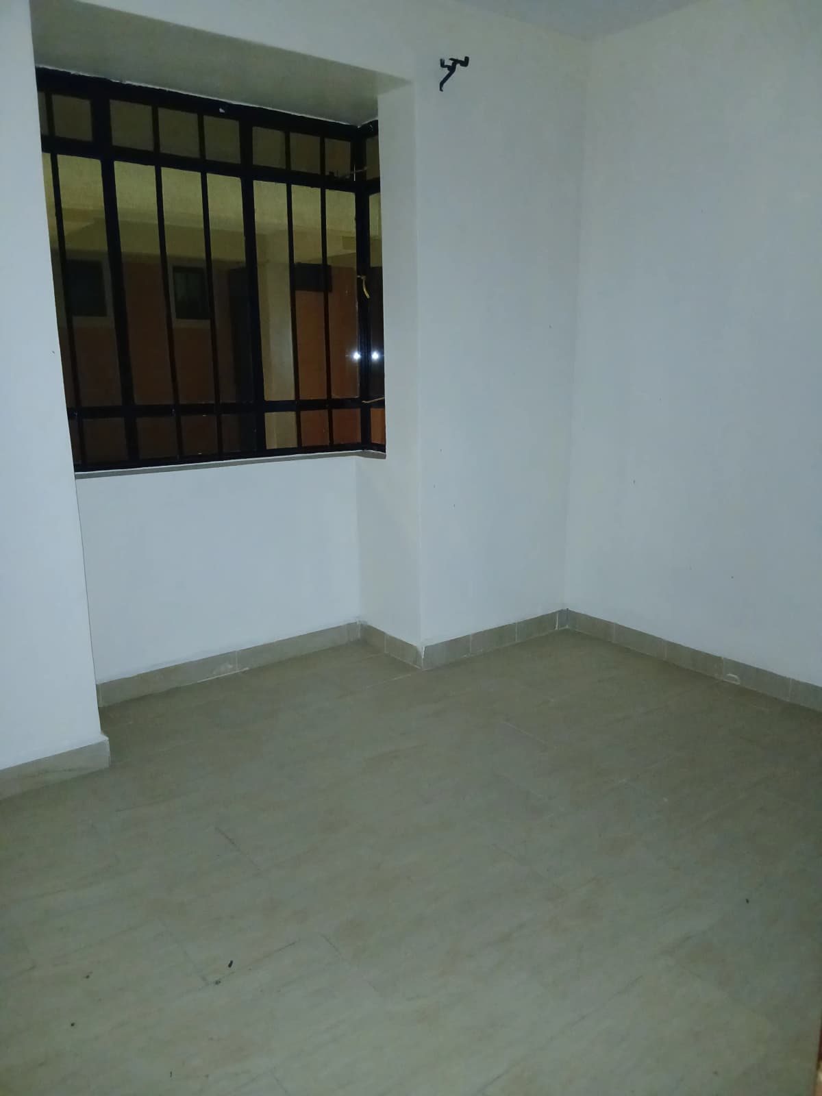 Empty bedroom with barred window and concrete flooring