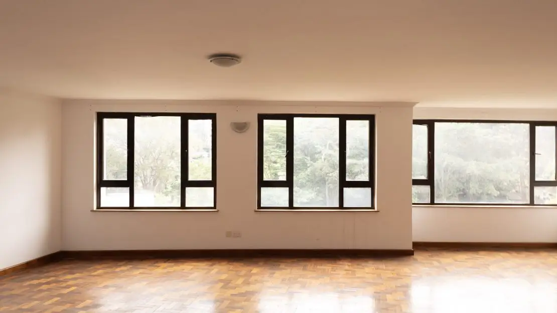 Spacious empty living room with parquet flooring and large windows.
