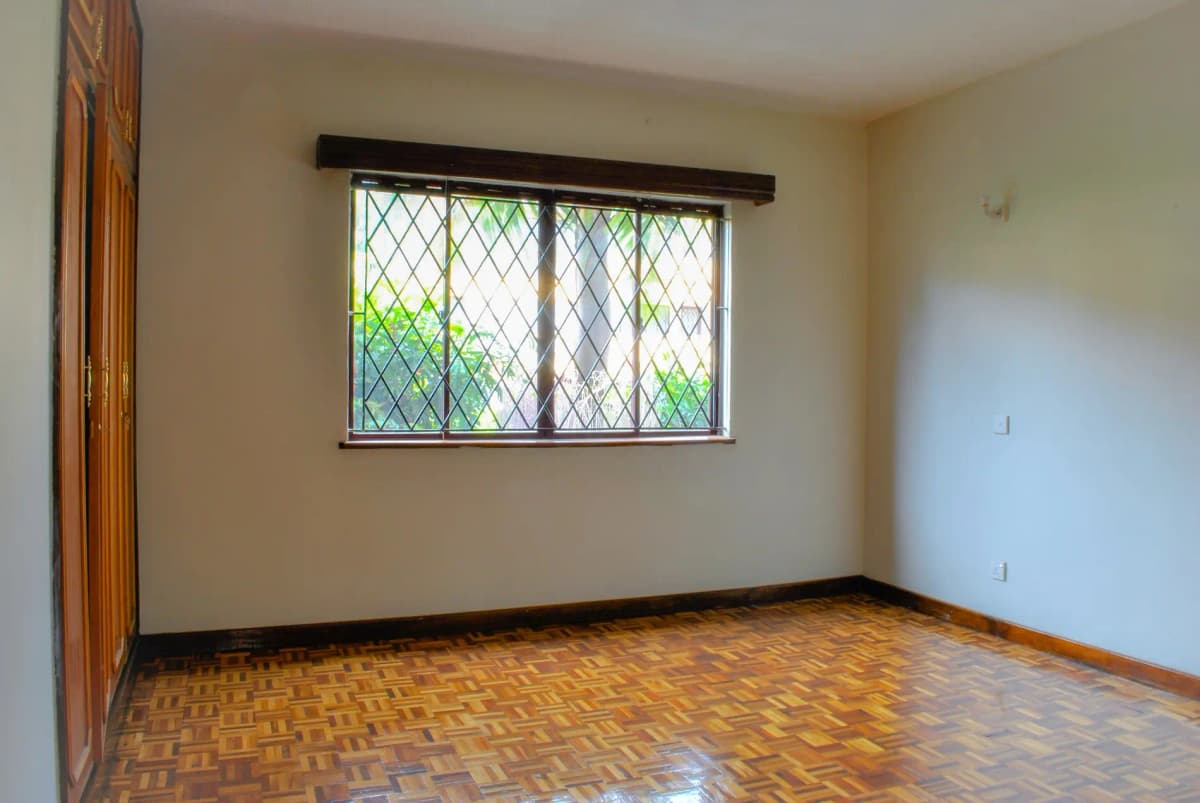 Spacious bedroom with wooden parquet flooring and barred window