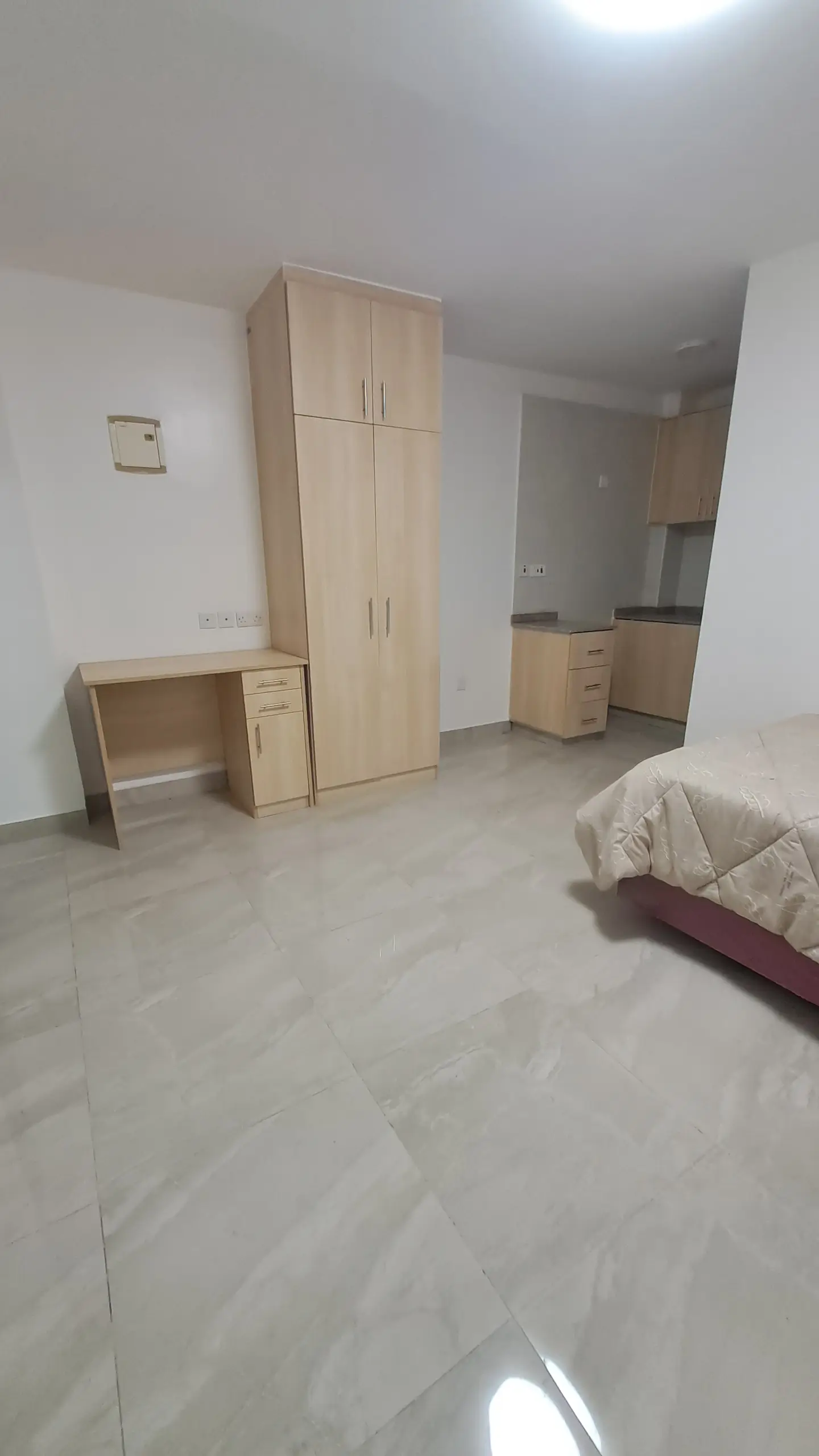 Bedroom with wooden wardrobes, open-plan kitchenette visible