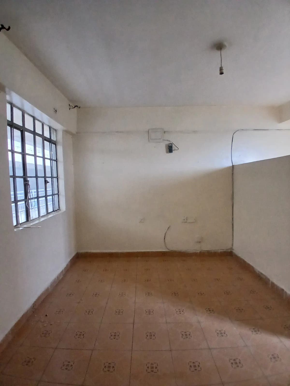 Unfurnished bedroom with barred window and terracotta tile floor