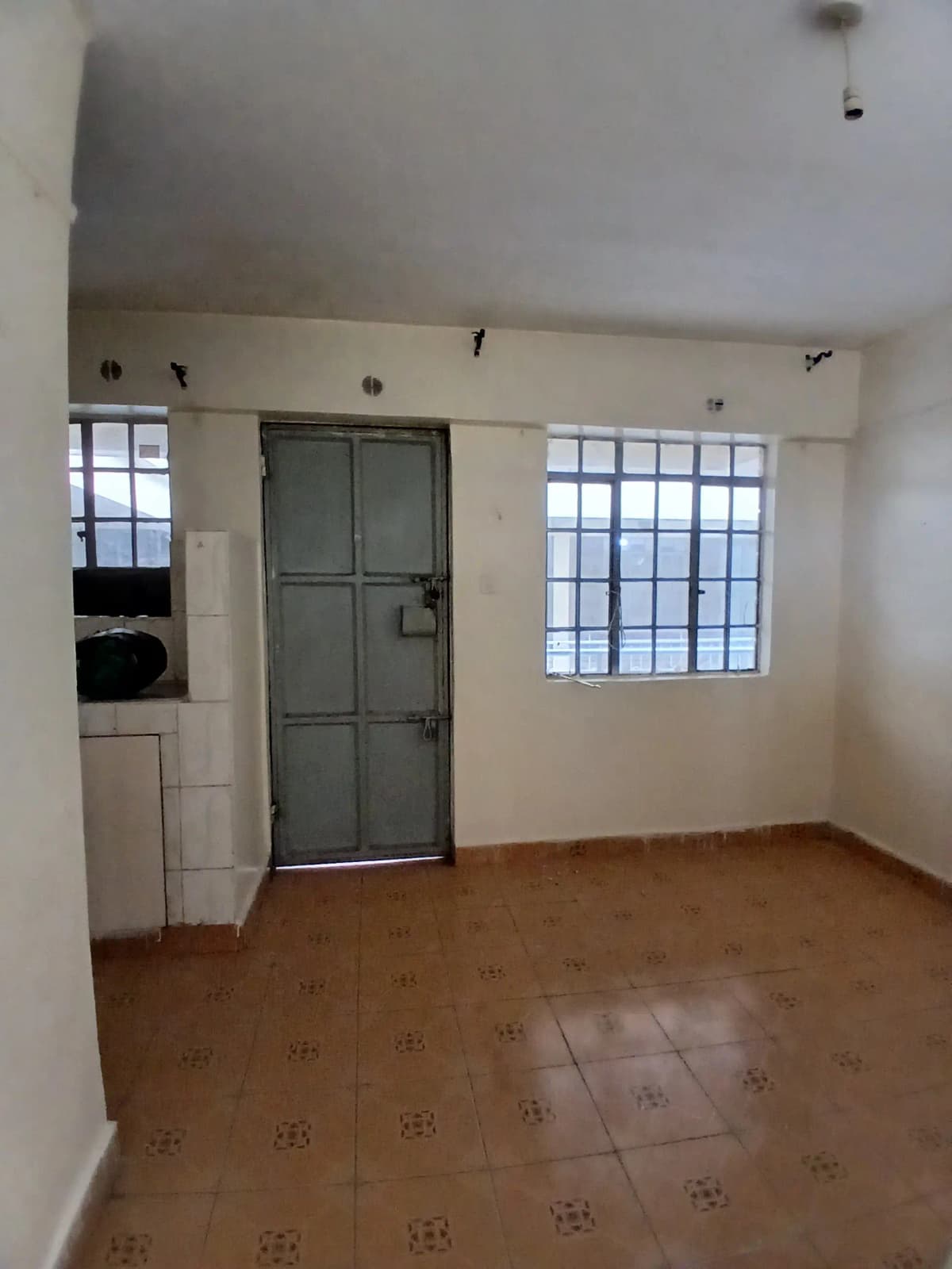 Sparse living room with terracotta tile floor and barred windows