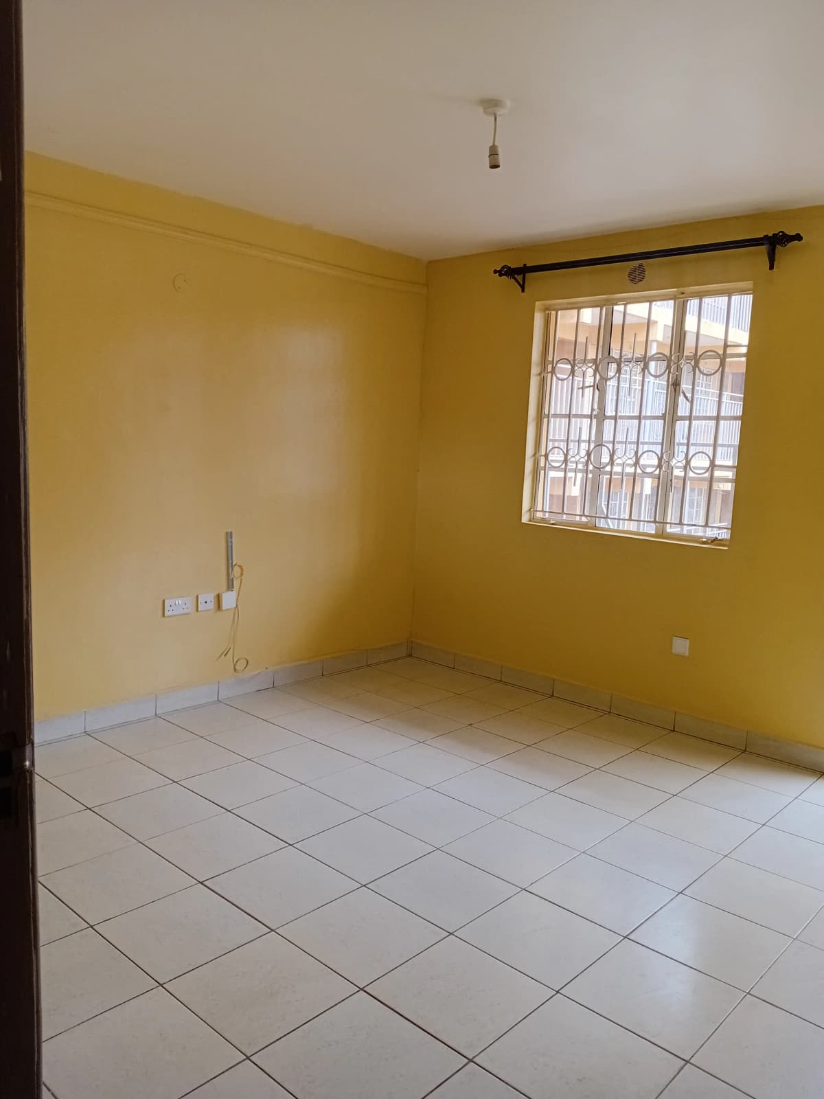 Bright yellow bedroom with tiled floor and barred window
