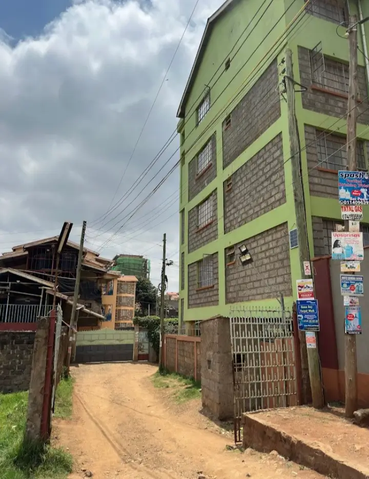 Green-painted multi-story residential building with dirt compound entrance