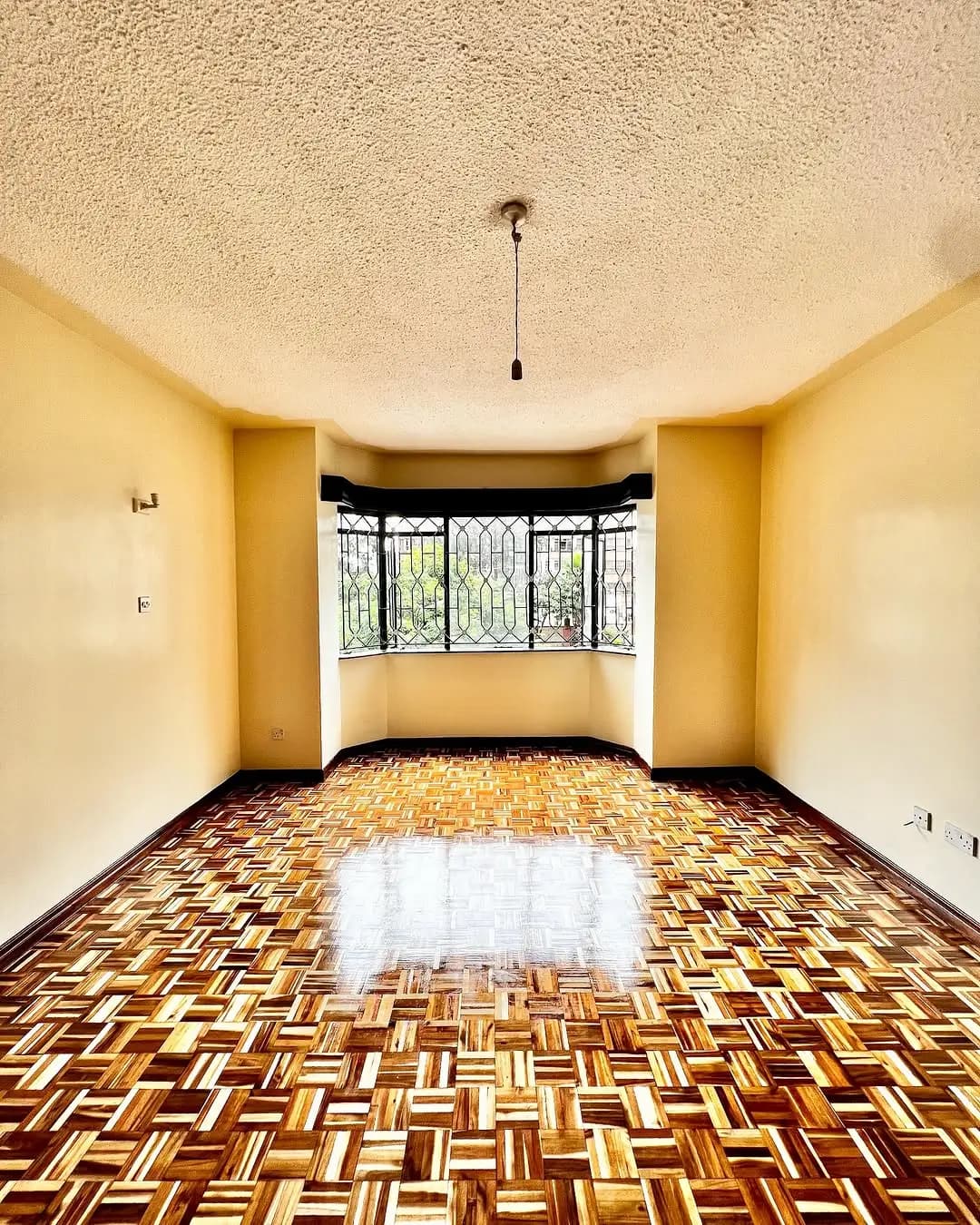 Bright yellow living room with geometric parquet flooring and bay window