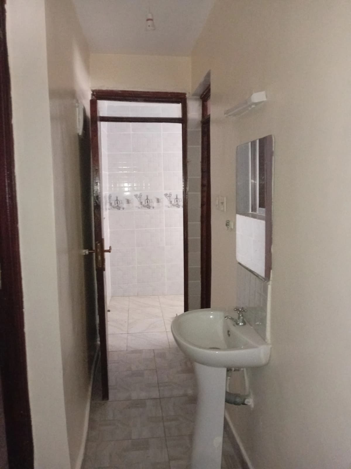 Narrow bathroom with pedestal sink and shower room beyond