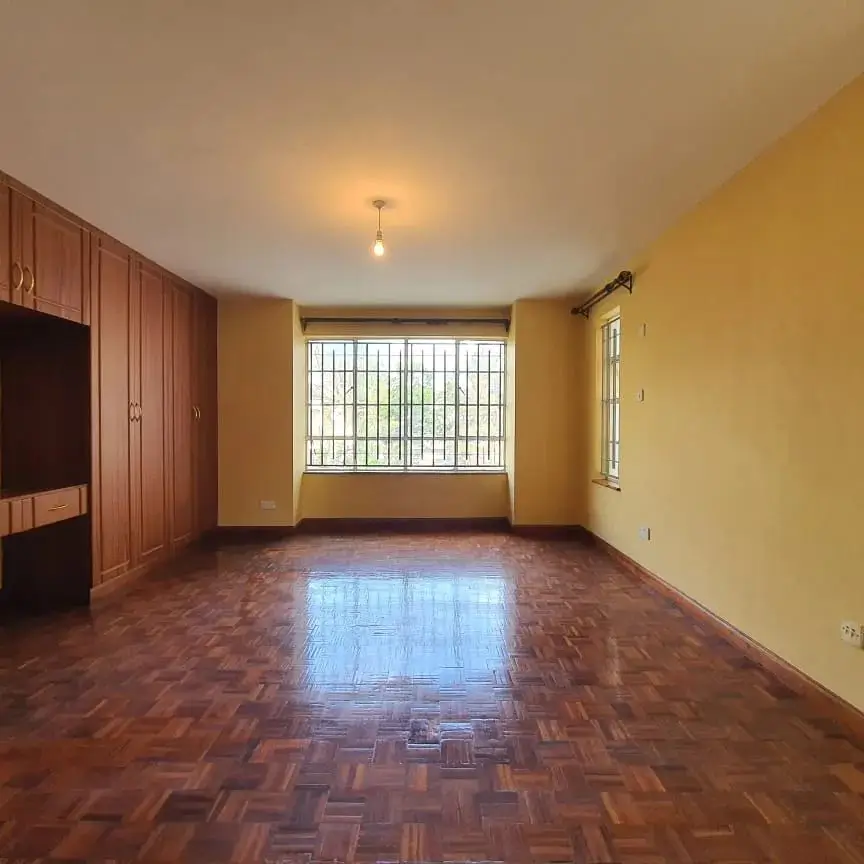 Spacious bedroom with wooden wardrobes and barred window