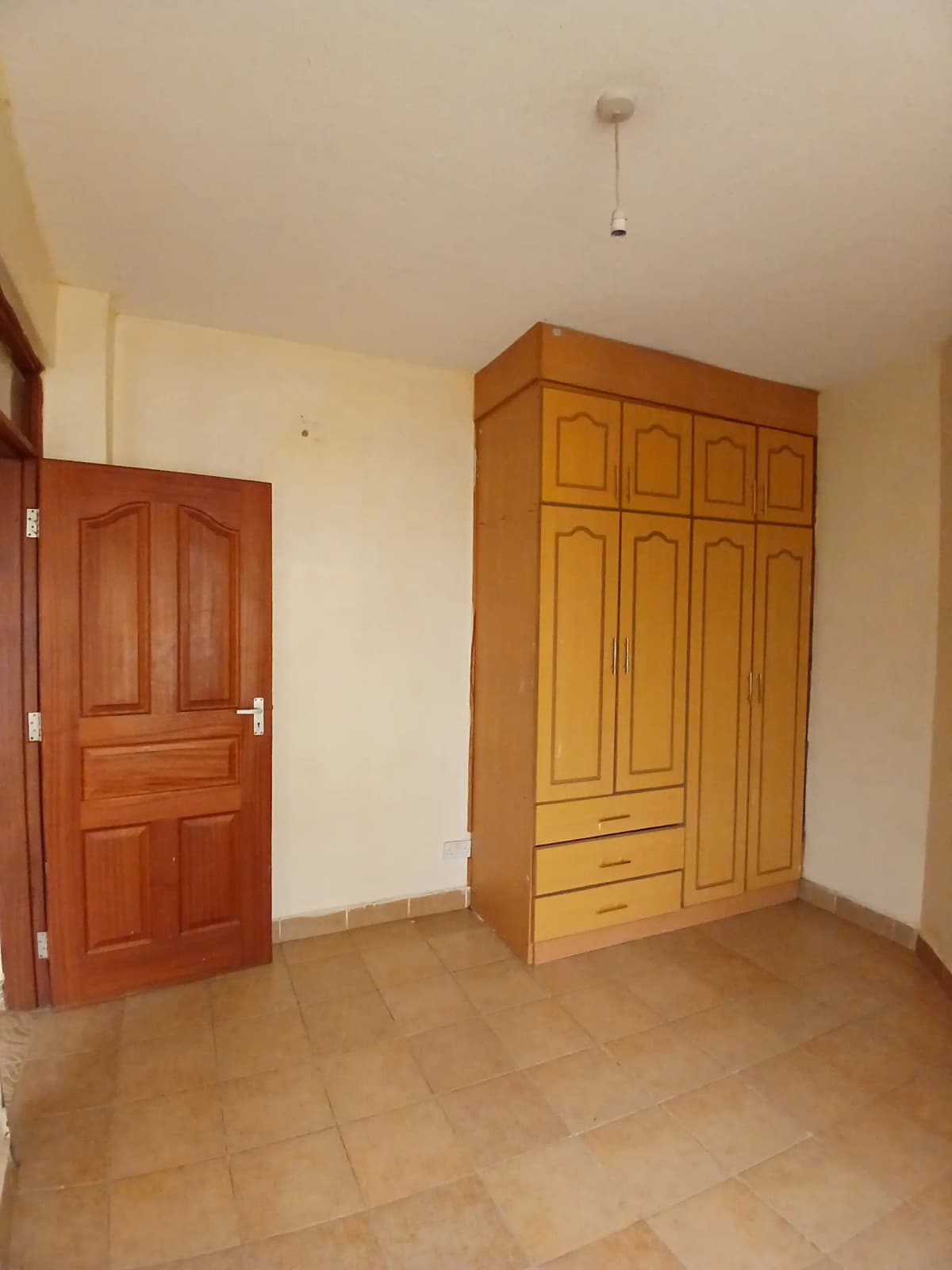 Spacious bedroom with wooden wardrobe and terracotta flooring