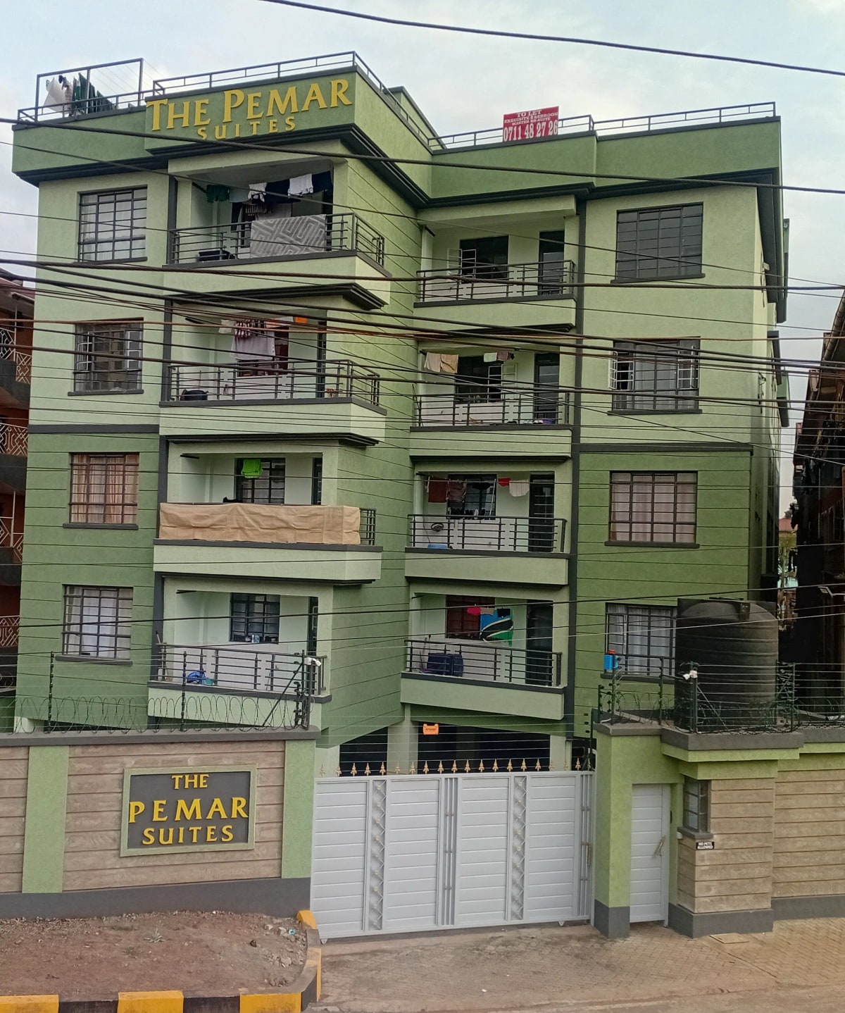 Multi-story green apartment building with street frontage and gates