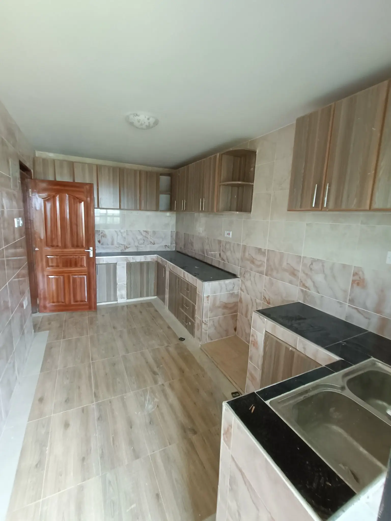 Modern kitchen with wooden cabinetry, black countertops, dual sink