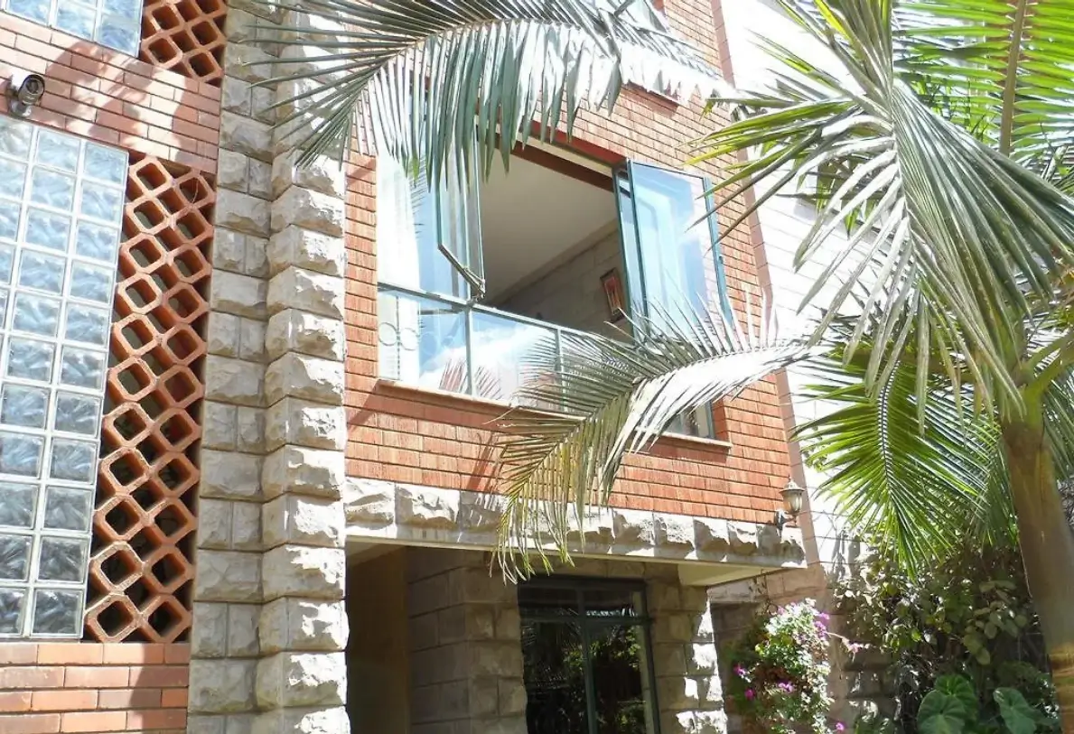 Red brick building facade with balconies and tropical plants