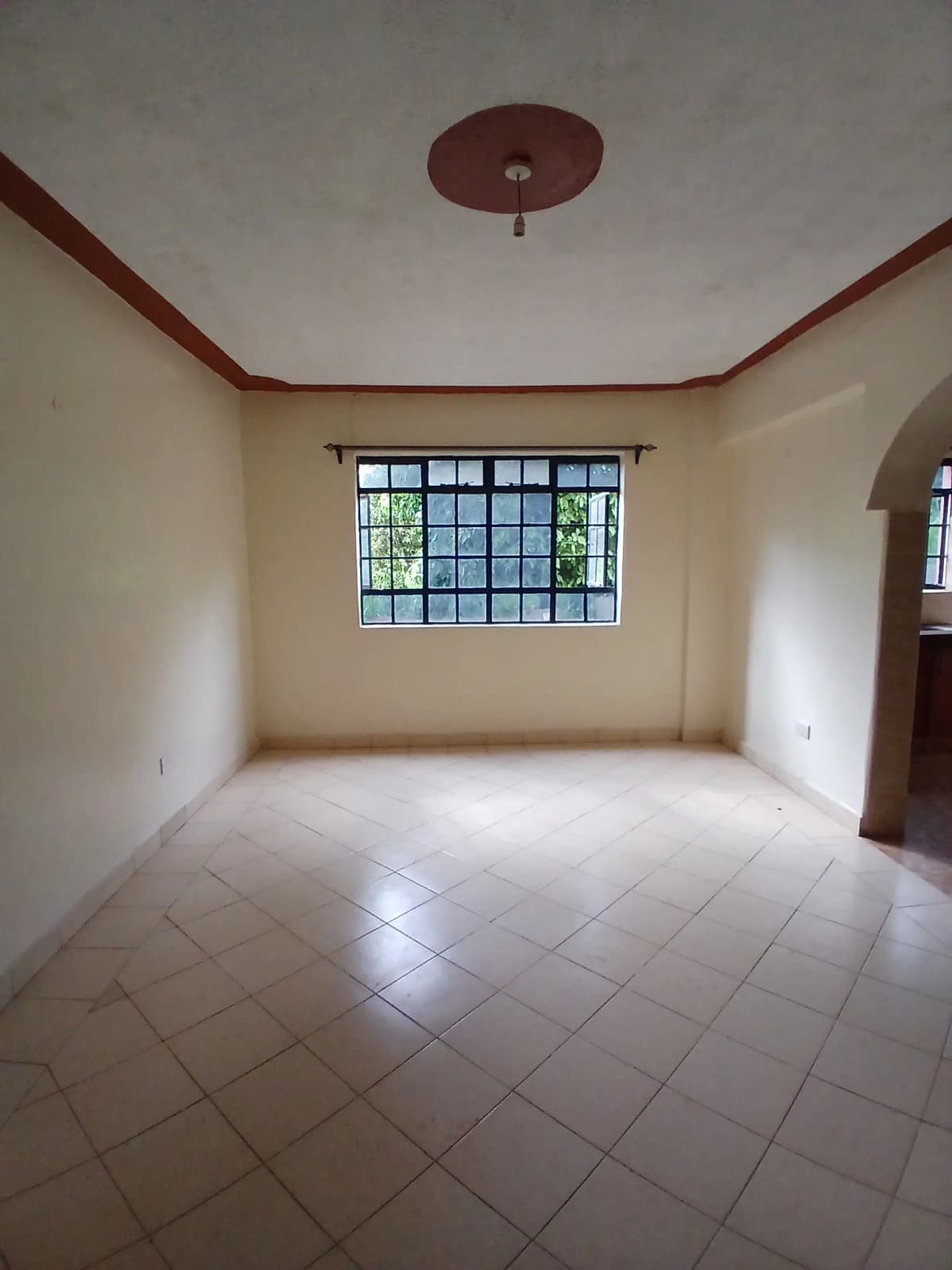 Spacious empty bedroom with barred window and red-trimmed ceiling