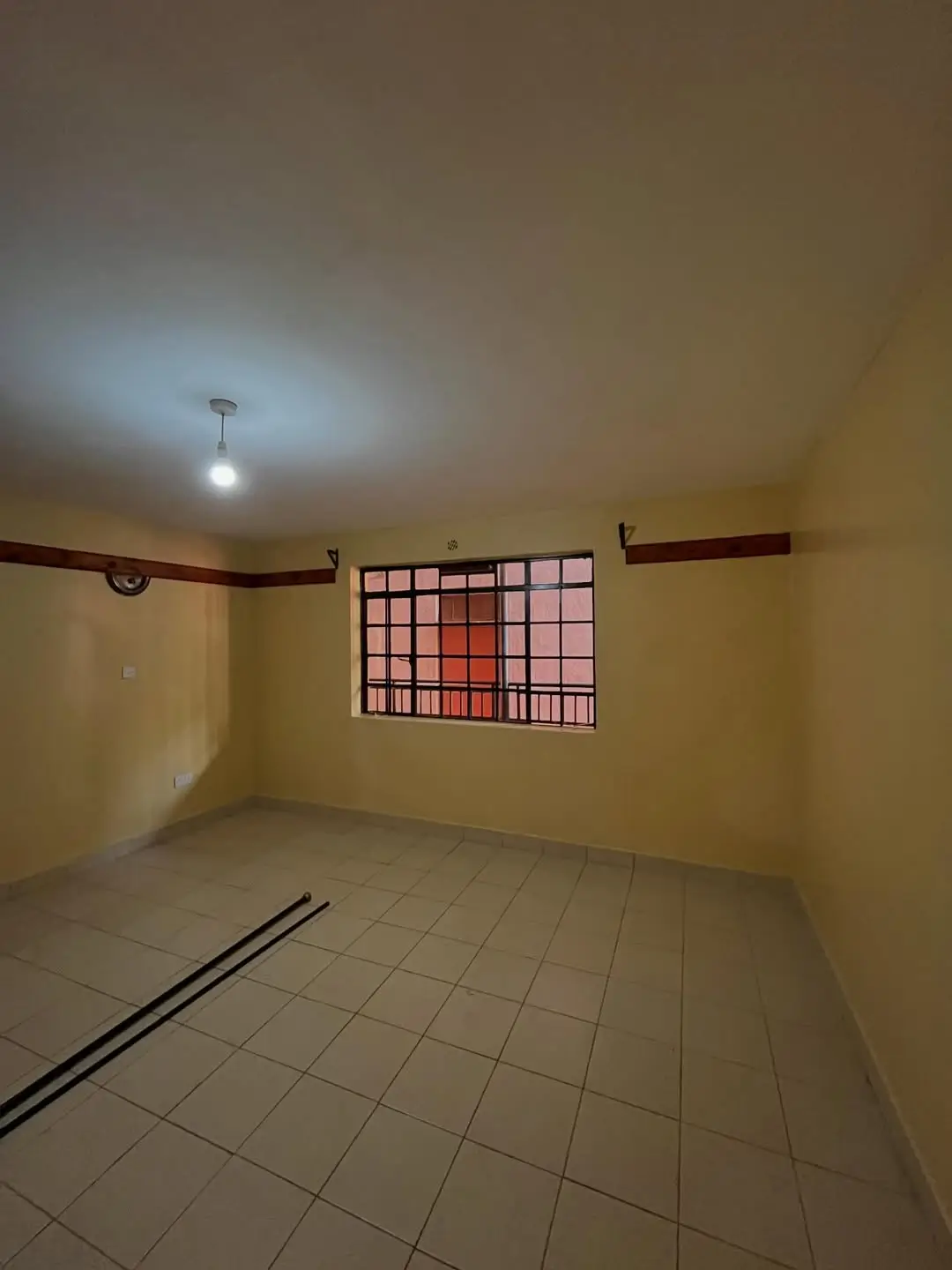 Spacious empty bedroom with tiled floor and window bars