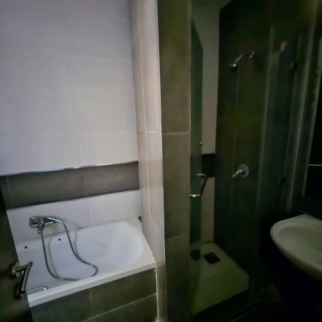 Compact bathroom with bathtub, shower enclosure, and green tile walls