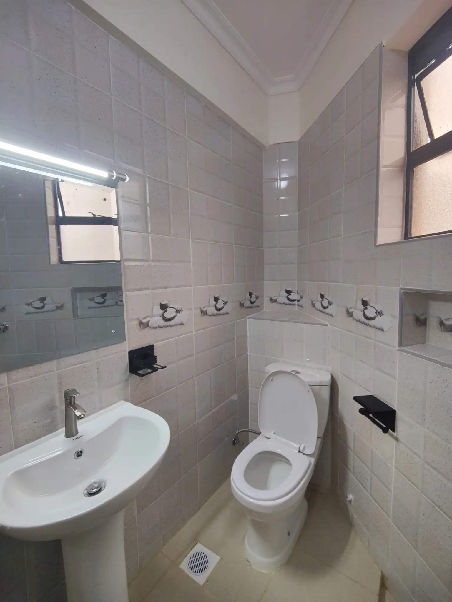 Clean bathroom with pedestal sink, toilet, and tiled walls